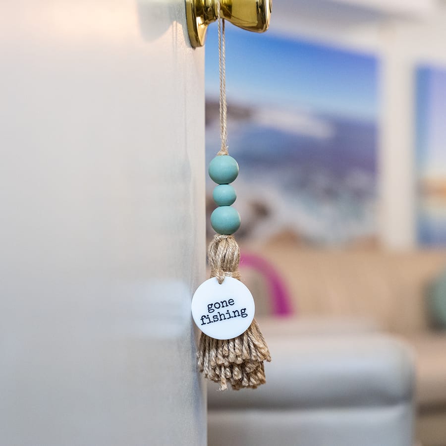 A jute and blue beaded tassel hanging from the office doorknob, its tag reading gone fishing