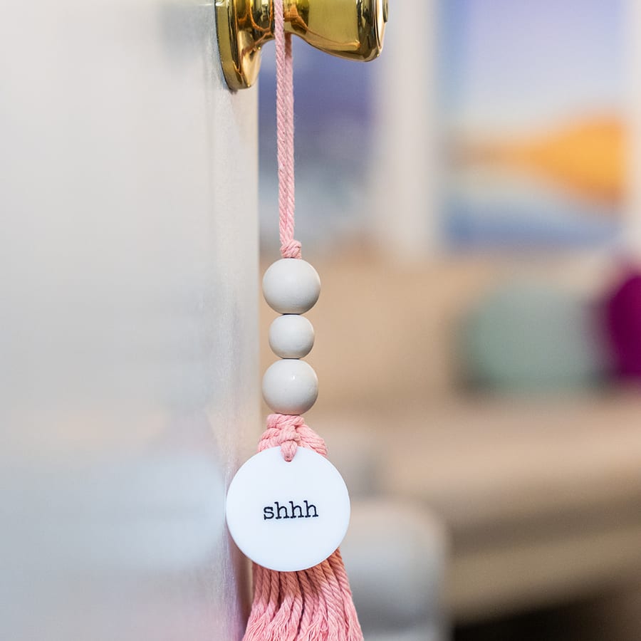 A pink beaded tassel hanging from the office doorknob, its tag reading shhh