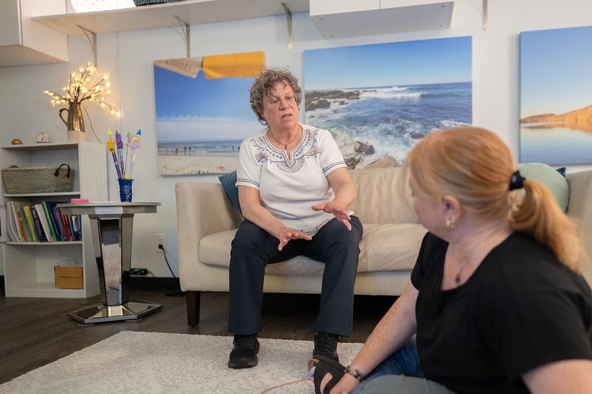 Karen Sussan sitting forward on the sofa in her Suffern office, talking and gesturing with both hands
