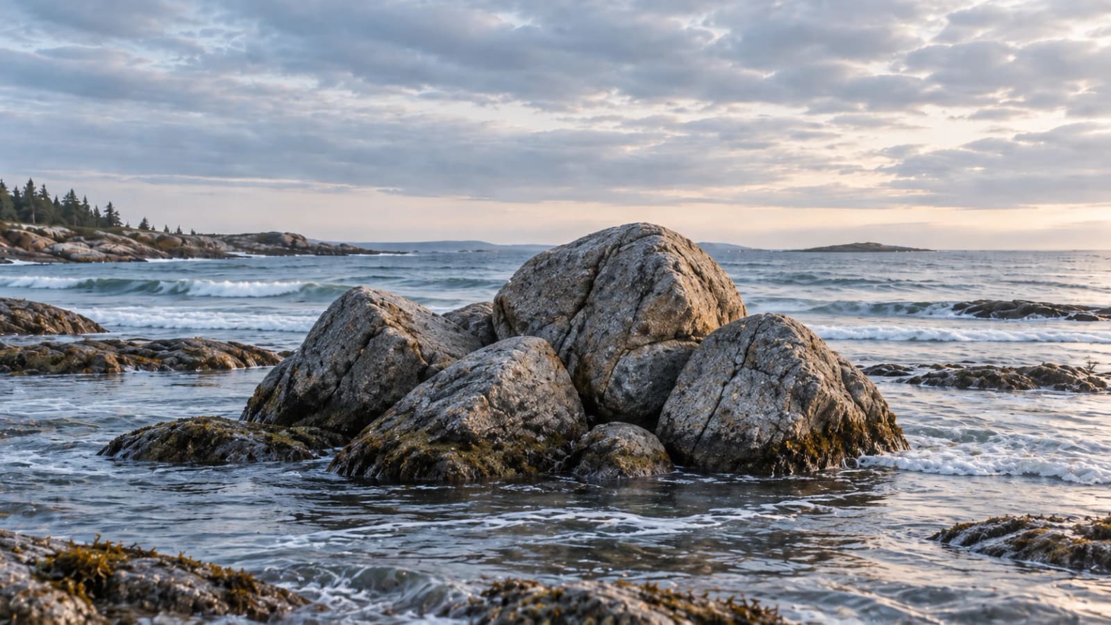 A cluster of granite boulders standing together in the shallows as the tide moves around them