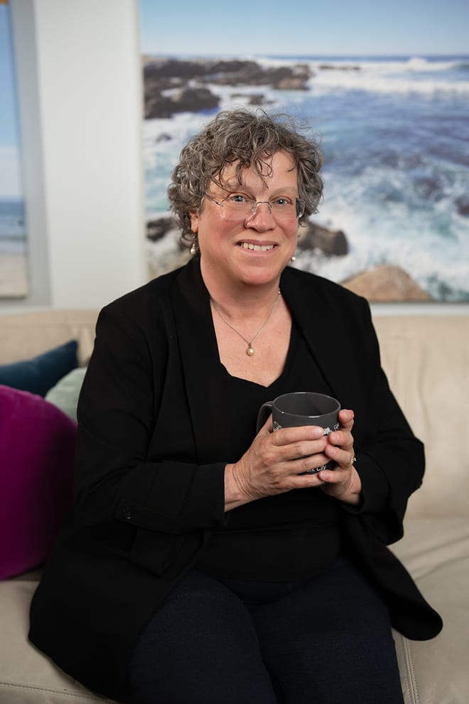 Karen Sussan, LCSW, LMHC, seated in her Suffern office holding a mug