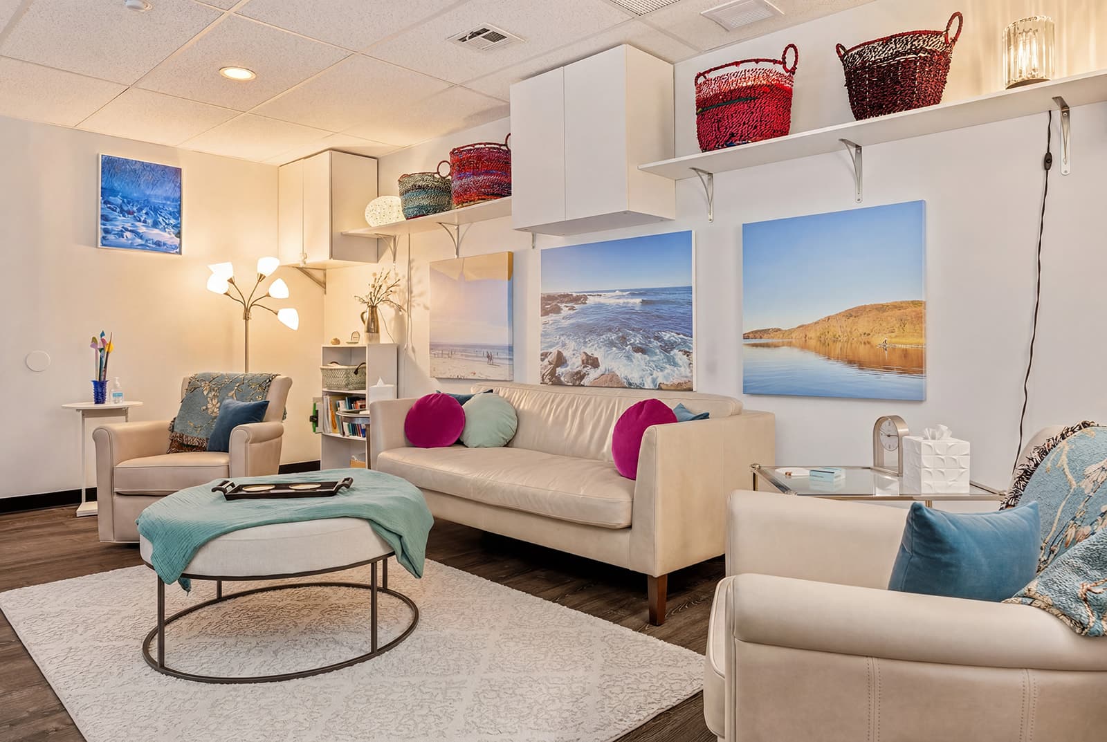 Karen Sussan's office in Suffern, NY, seen from the doorway: a sofa and armchairs around a low ottoman, with coastal canvases on the walls